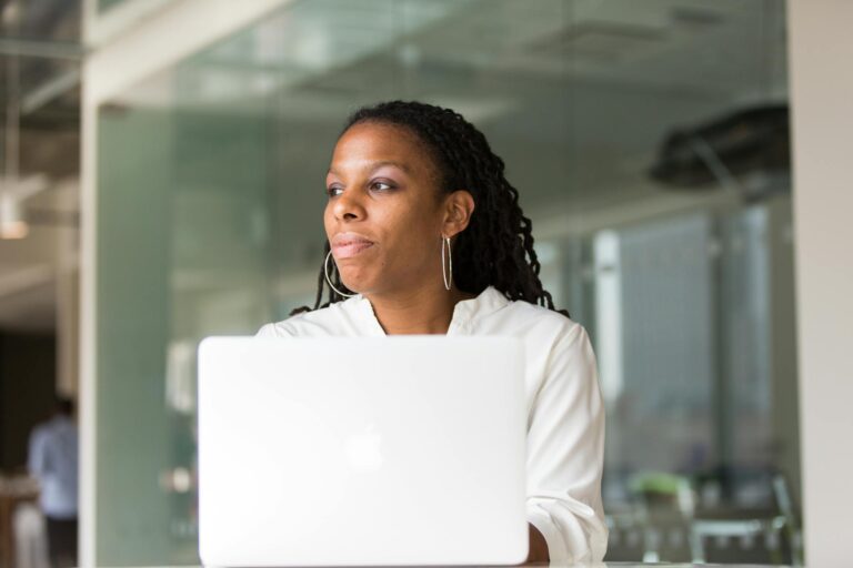 A professional black woman concentrating on work using a laptop in a modern office setting.